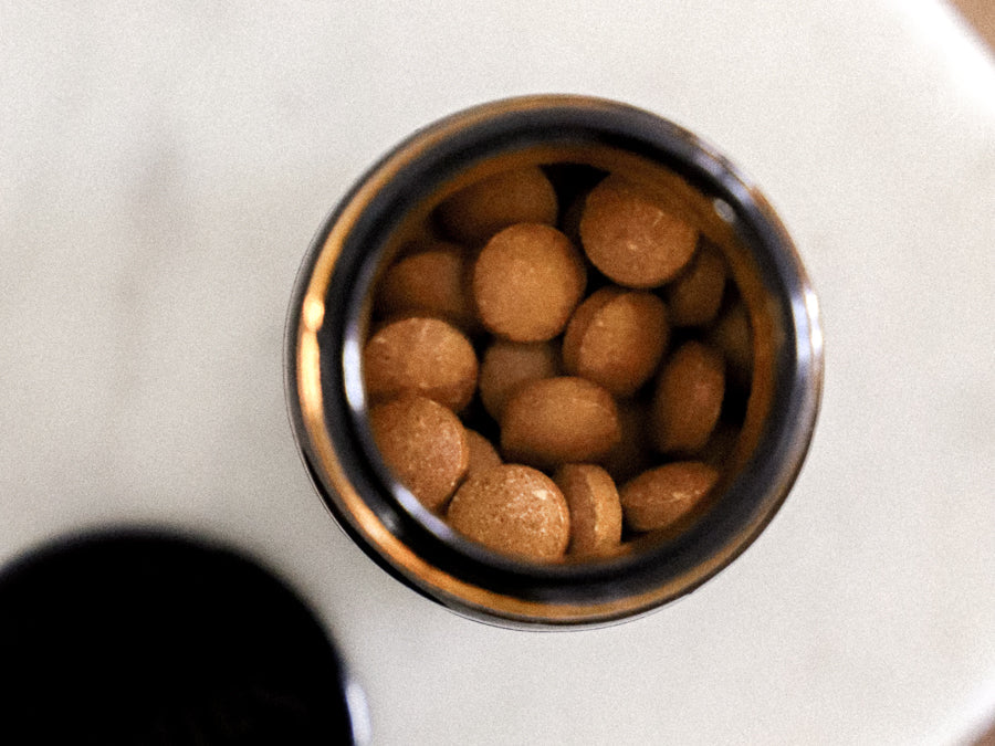 Overhead view of Sanbera Daily Essential Men tablets in an open amber glass jar on a light surface.